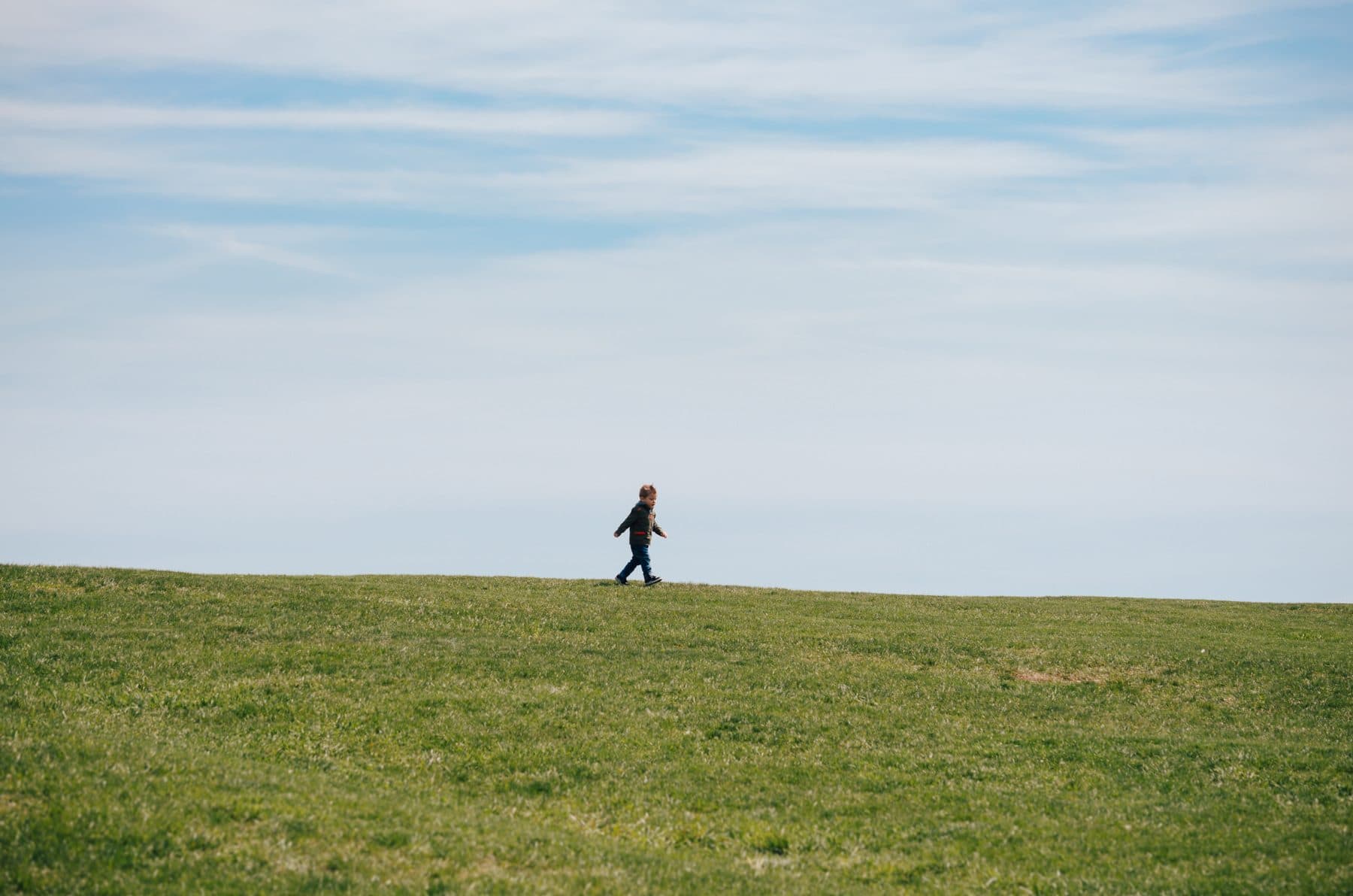 A distant runner crossing a wide green field
