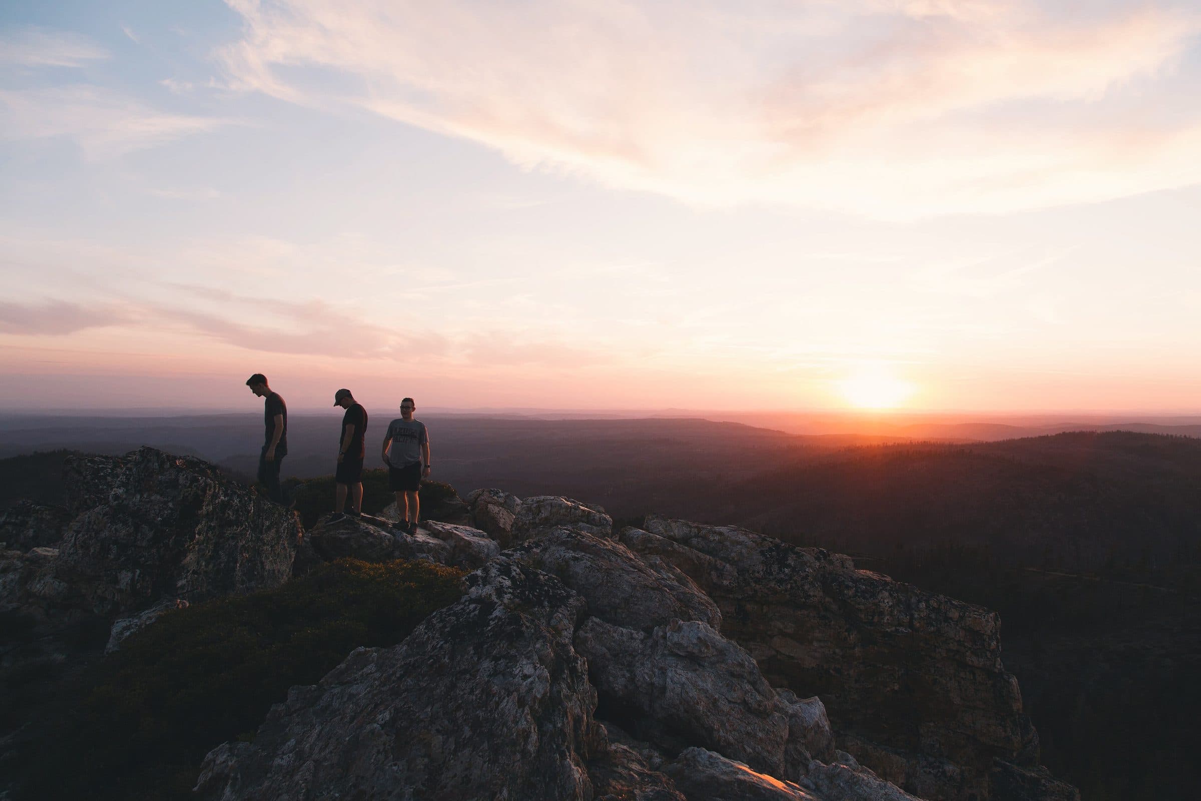 Three people in silhouette watching a sunrise from rocks